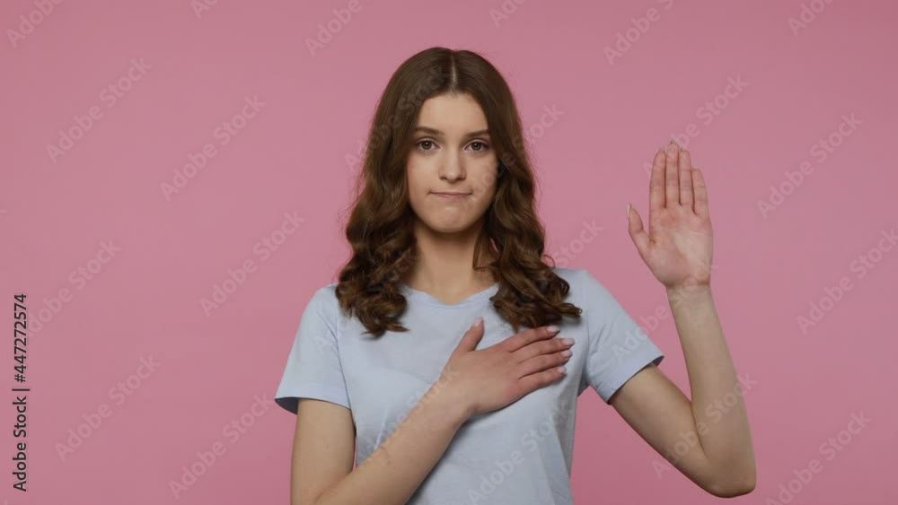 I swear! Sincere teenager girl with wavy hair raising hand to promise, taking vow with serious expression, giving oath to be faithful. Indoor studio shot isolated over pink background. I swear! Sincere teenager girl with wavy hair raising hand to promise, taking vow with serious expression, giving oath to be faithful. Indoor studio shot isolated over pink background.