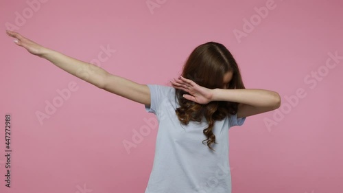 Satisfied joyful teenager girl in T-shirt celebrating success with dab dance move, famous internet meme of triumph, performing dabbing trends. Indoor studio shot isolated over pink background. photo