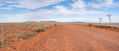 Unsealed Outback road, remote travel. Ultra wide panorama, South Australian landscape. Dirt  road access to remote Outback communities and Stations.