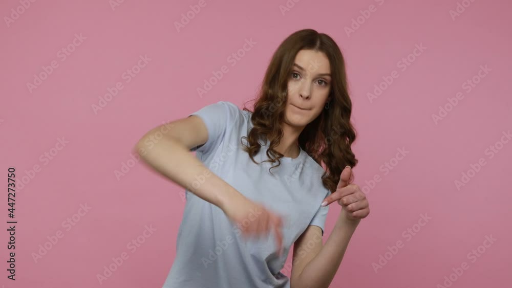 Happy girl with dark wavy hair in casual T-shirt pointing fingers down, demanding doing something right now, looking excited, indicating hither. Indoor studio shot isolated over pink background. Happy girl with dark wavy hair in casual T-shirt pointing fingers down, demanding doing something right now, looking excited, indicating hither. Indoor studio shot isolated over pink background.