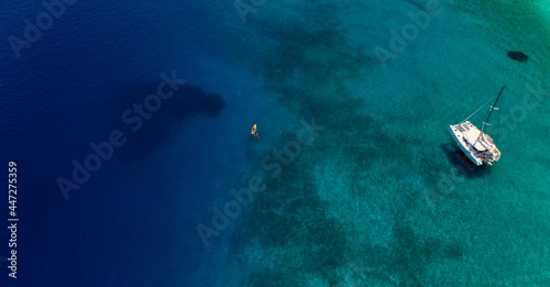 Aerial shot of people next to a yellow water board close to a moored catamaran at the turquoise sea of Gidaki beach in Itaca, Greece
