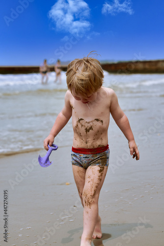 A little boy gets dirty in mud and walks crying along the beach