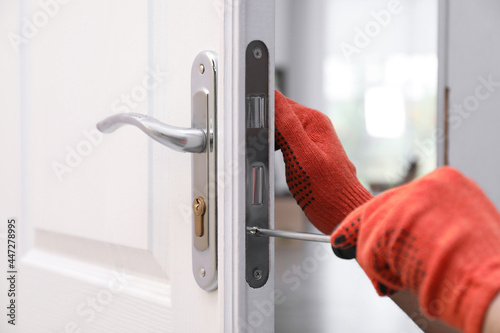 Handyman with screwdriver repairing door lock indoors, closeup photo