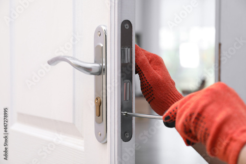 Handyman with screwdriver repairing door lock indoors, closeup