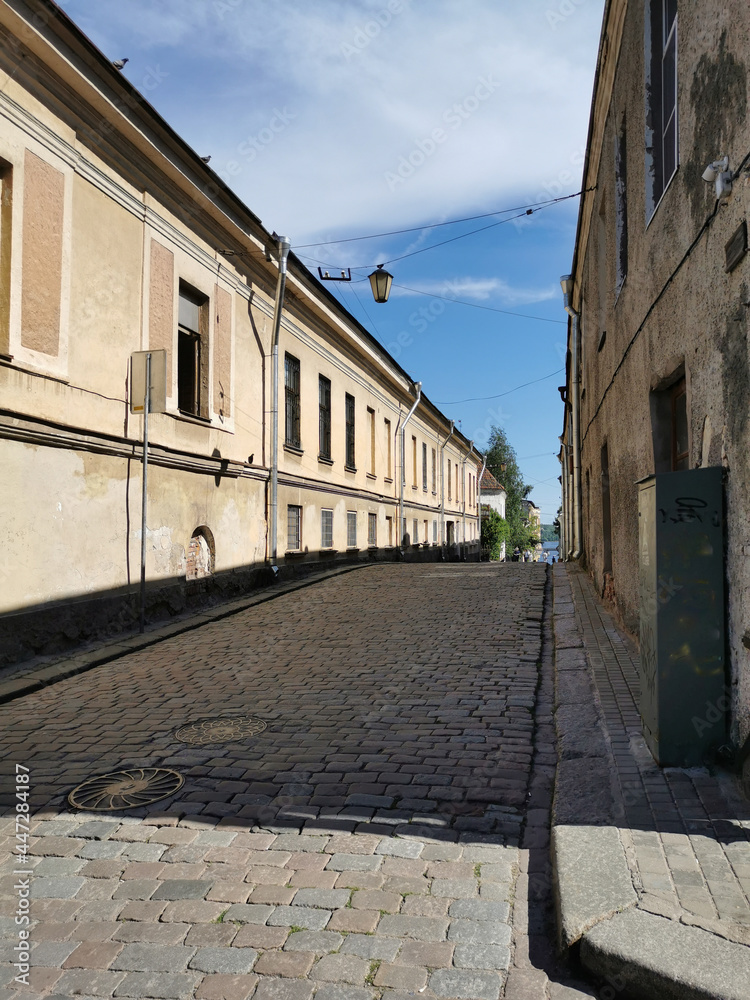 A cobbled, narrow, ancient street of the city of Vyborg on a sunny summer day.