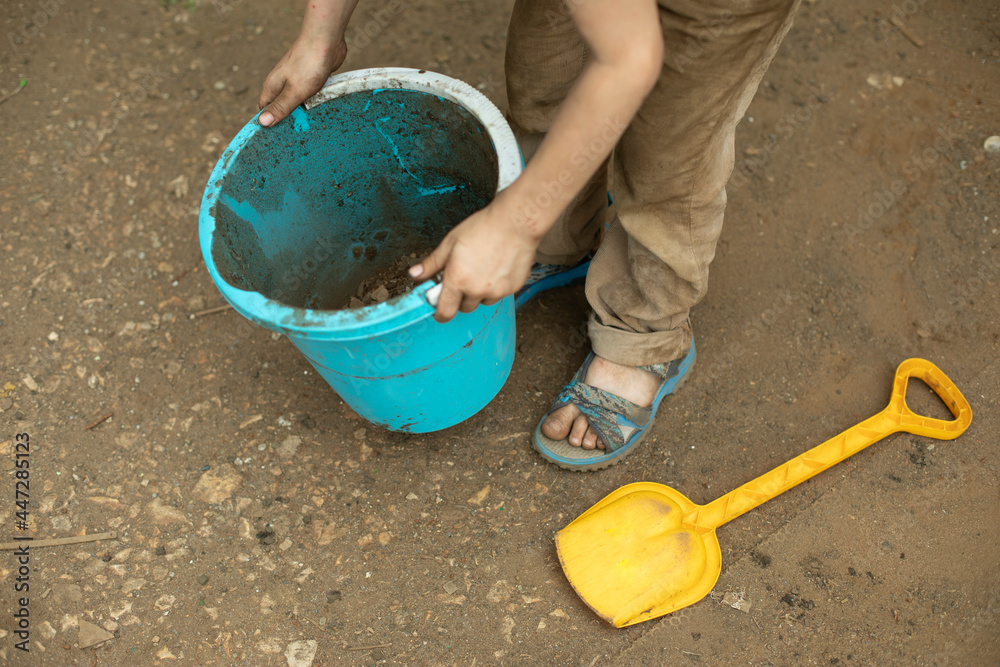 The child is holding a bucket. Blue bucket in hand. The child is holding a bucket. Blue bucket in hand.