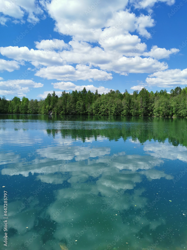 Fototapeta premium The shore of the lake is bright with clear water, in which you can see the marble on the bottom and reflect the sky with clouds, in the mountain park Ruskeala.