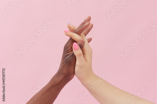 Caucasian woman and African-American man holding hands together on pink background. Racism concept