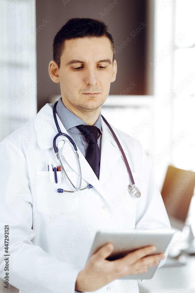 Friendly male doctor using tablet computer in sunny clinic. Medicine and healthcare concept Friendly male doctor using tablet computer in sunny clinic. Medicine and healthcare concept