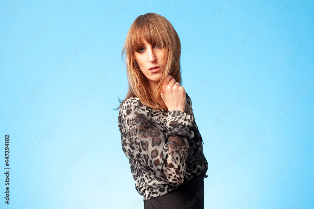 Fototapeta premium Portrait of a beautiful brunette woman wearing a leopard animal print blouse against a blue background