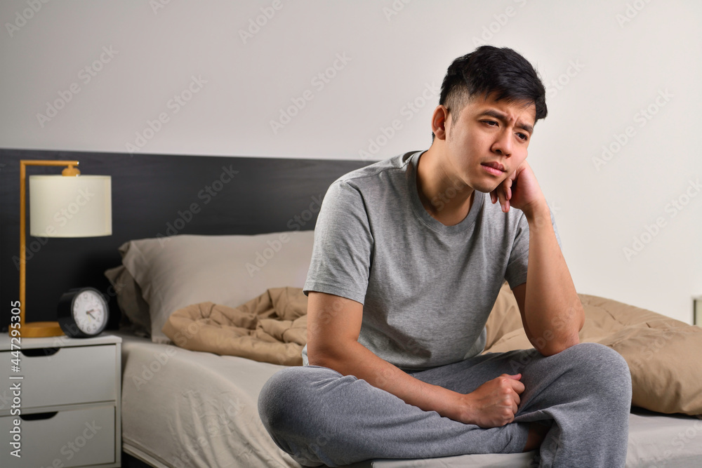 Depressed young Asian man sitting in bed cannot sleep from insomnia