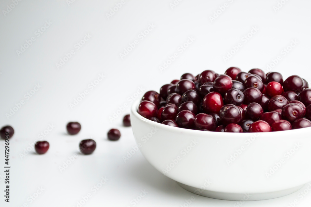 Dark red cherry in a white cup on a white background. And scattered cherries nearby. Dark red cherry in a white cup on a white background. And scattered cherries nearby.