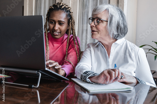 Multiracial senior and young woman using laptop computer at home - Focus on right face photo
