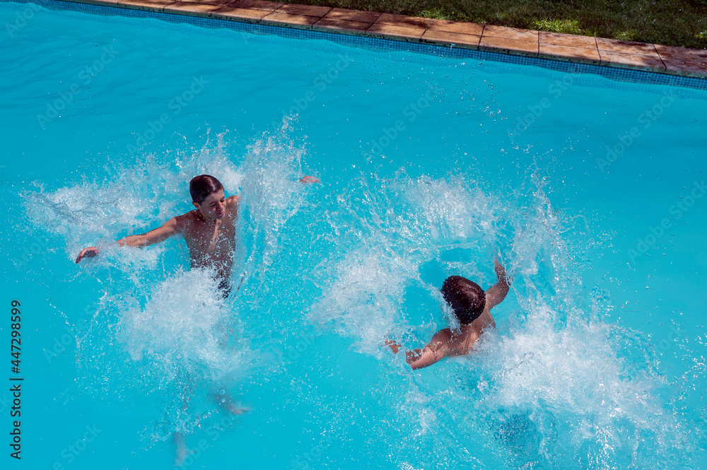 Deux garçons adolescents qui jouent à sauter dans l'eau d'une piscine en extérieur en été