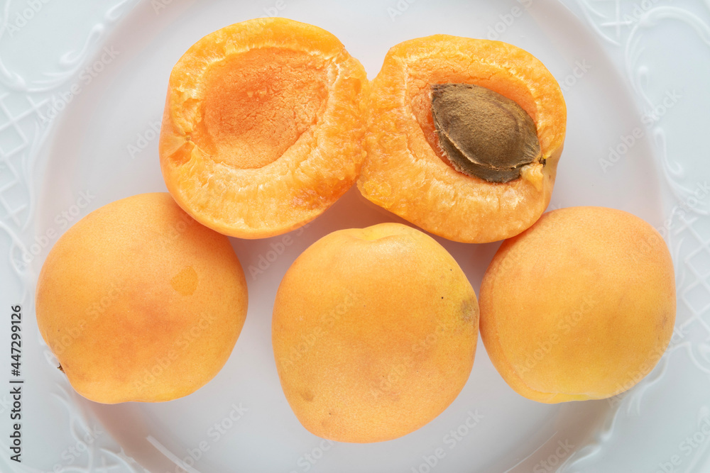 Three whole and two half ripe apricots on a white earthenware dish, close-up, top view.
