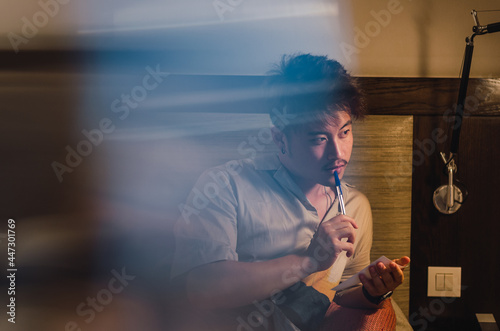 Young relaxed asian man traveller using smartphone, computer and taking notes in hotel room while on vacation