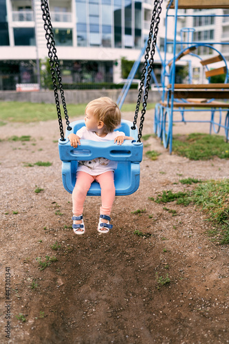 Little girl sitting on a swing in the playground, turning her head back