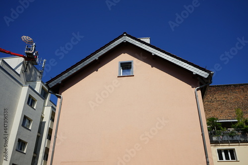 Glatte Fassade in einem angenehmen Pastellton mit Giebelfenster und Spitzgiebel vor blauem Himmel bei Sonnenschein im Nordend von Frankfurt am Main in Hessen