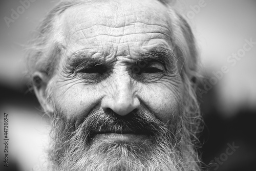 Close - up of wrinkled face of old senior man portrait with white hair and a white beard, black and white