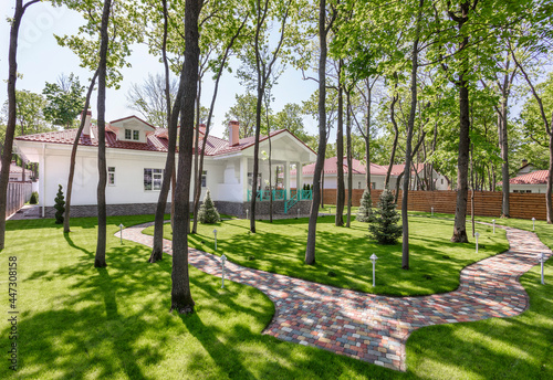 Backyard of modern white country house with brown roof and beautiful garden. Well-groomed beautiful lawn. Space for text. High quality photo