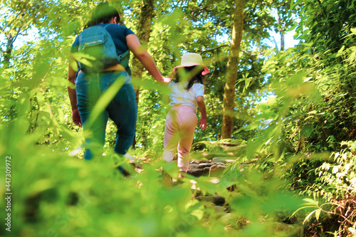 una mama caminando por un sendero rodeado de naturaleza de la mano de su hija, enseñándole la importancia de la naturaleza. 