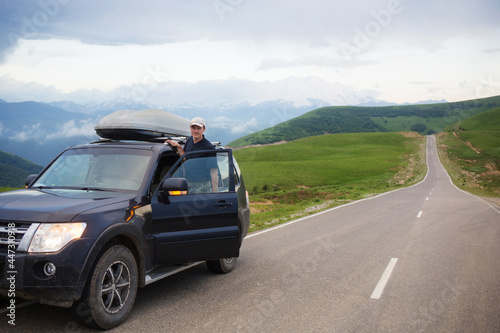 man male driver stands on running board of SUV car against background of asphalt road and mountain landscape. travel, trip in summer © Natalia