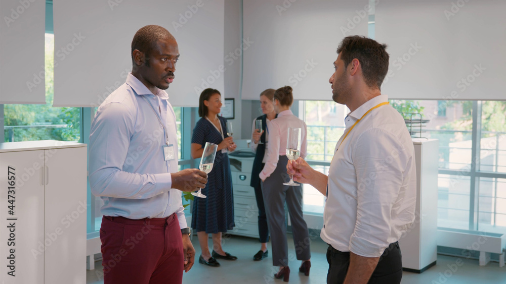 Fototapeta premium Side view of cheerful multicultural businessmen holding champagne glasses and talking in office