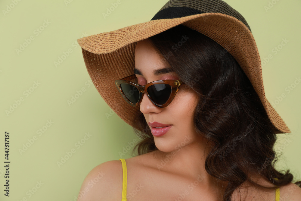Beautiful young woman with straw hat and stylish sunglasses on light green background Beautiful young woman with straw hat and stylish sunglasses on light green background