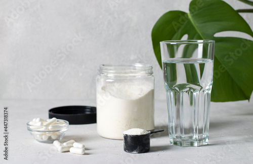 Cuadro en lienzo Collagen powder in a jar and measuring spoon, collagen capsules and a glass of water on a gray background with monstera leaf