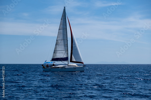 Sailing boat with open white sails, blue sky and rippled sea background