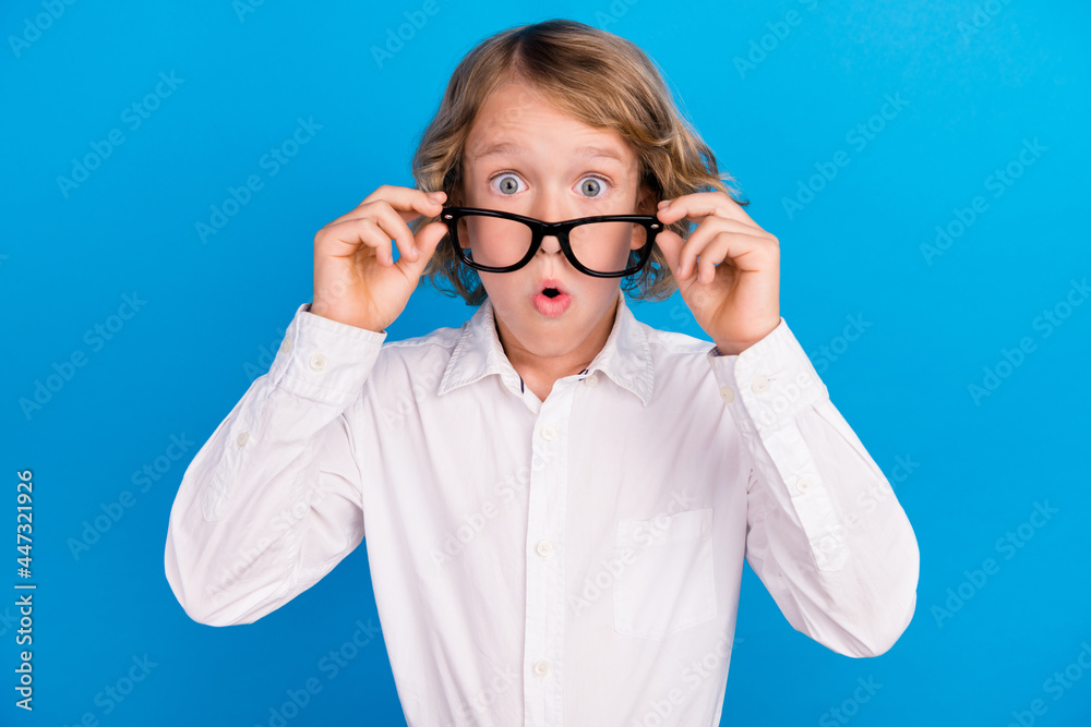 Portrait of attractive amazed boy touching specs pout lips incredible news isolated over vibrant blue color background