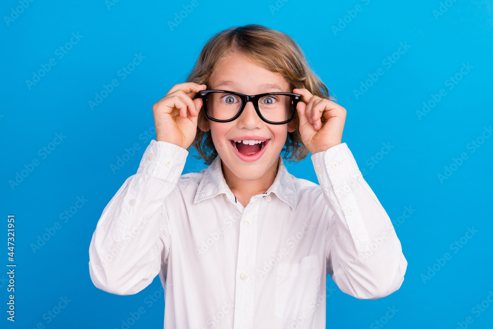 Portrait of attractive cheerful amazed boy touching specs having fun isolated over vibrant blue color background Portrait of attractive cheerful amazed boy touching specs having fun isolated over vibrant blue color background