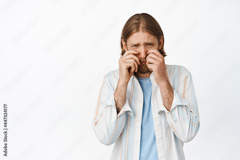 Portrait of silly and sad blond guy feeling timid, adult man crying and looking upset, wiping tears and rub eyes depressed, standing against white background Portrait of silly and sad blond guy feeling timid, adult man crying and looking upset, wiping tears and rub eyes depressed, standing against white background