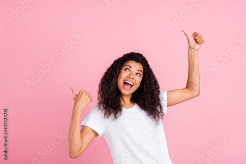 Photo of pretty sweet dark skin woman dressed white t-shirt looking empty space showing thumbs up isolated pink color background © deagreez