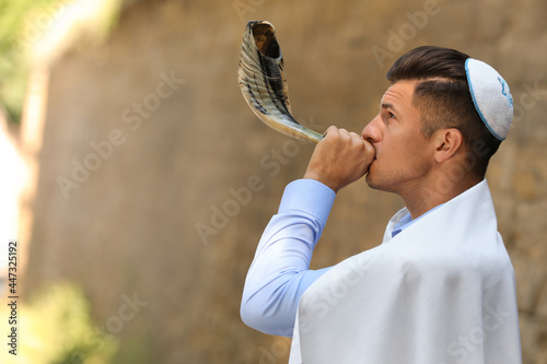 Jewish man in kippah and tallit blowing shofar outdoors. Rosh Hashanah celebration photo