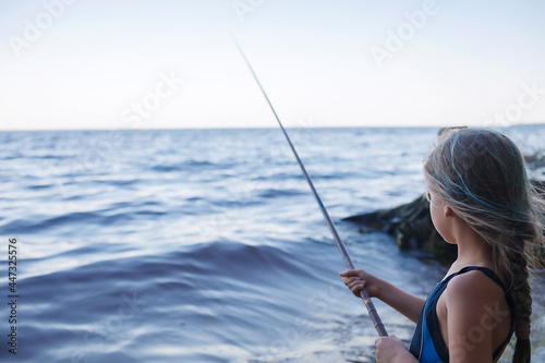 Pretty girl in swimming wear fishing from sea beach in early morning, blue hours, active weekend and camping, outdoors lifestyle