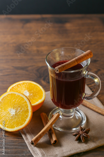 Mulled wine in glass cups with cinnamon and oranges on a wooden table.