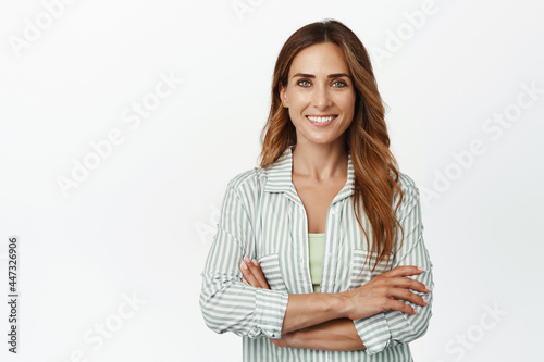 Ambitious and confident business woman, female entrepreneur standing with arms crossed and smiling self-assured at camera, saleswoman against white background