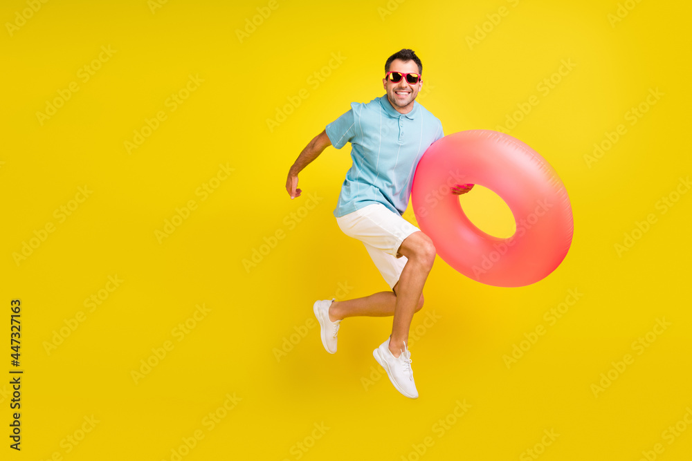 Photo of pretty sweet young guy dressed blue t-shirt dark eyewear running jumping holding inflatable ring isolated yellow color background Photo of pretty sweet young guy dressed blue t-shirt dark eyewear running jumping holding inflatable ring isolated yellow color background
