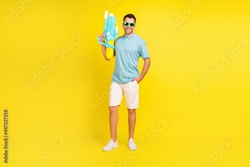 Full size photo of funny brunet man with gun wear t-shirt shorts isolated on yellow color background