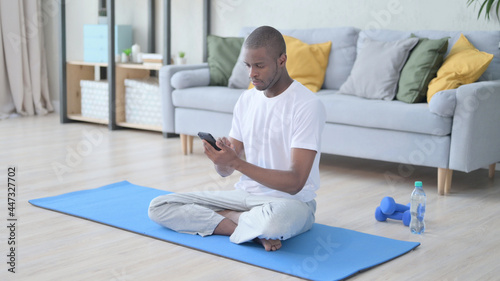 African Man using Smartphone on Yoga Mat at Home