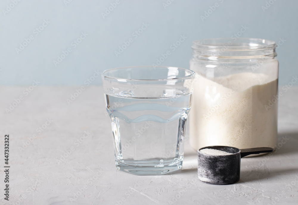 Glass of water, collagen powder in jar and a measuring spoon with powder on a light blue background with place for text Glass of water, collagen powder in jar and a measuring spoon with powder on a light blue background with place for text