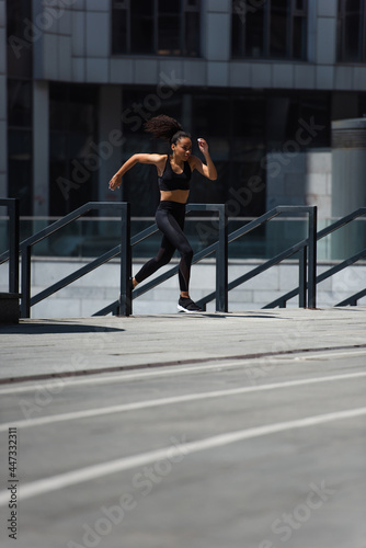 African american sportswoman running near railing on urban street