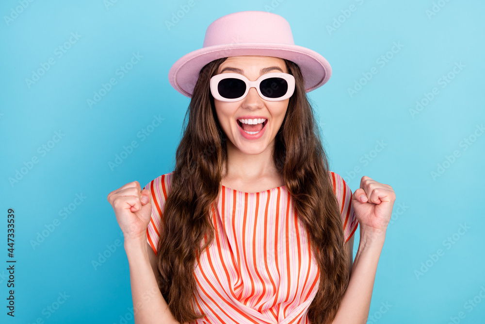 Photo of astonished crazy champion lady raise fists wear sunglass hat striped dress isolated blue color background Photo of astonished crazy champion lady raise fists wear sunglass hat striped dress isolated blue color background