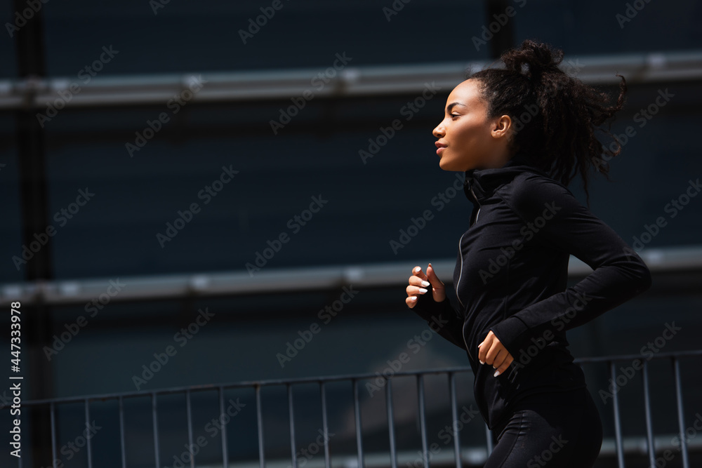 Side view of african american runner in sports jacket on urban street