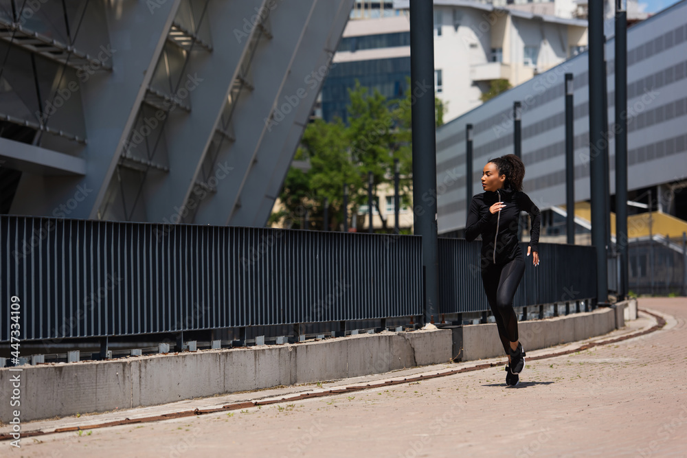 Side view of african american sportswoman running near building on urban street