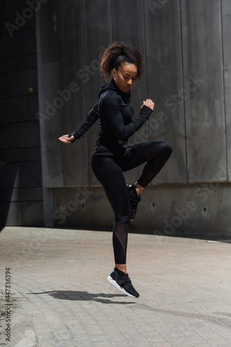 African american woman jumping while exercising on urban street