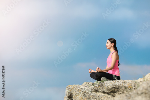 Young woman meditating on cliff. Space for text