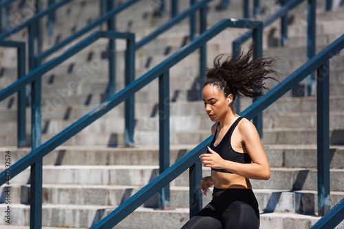 Fit african american sportswoman in earphone running on stairs