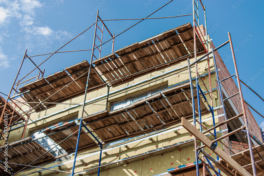 Thermal insulation of a red brick house with mineral wool. The use of scaffolding when building a house. Thermal insulation of a red brick house with mineral wool. The use of scaffolding when building a house.